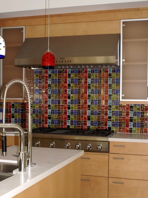 a light-stained kitchen with taupe upper cabinets, a colorful mosaic tile backsplash and colorful pendant lamps that echo with it