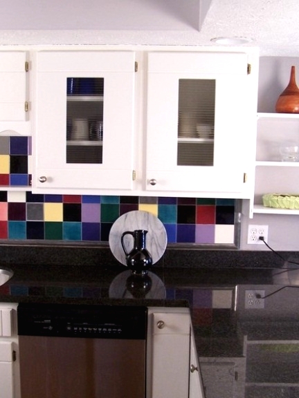 a white kitchen with dark grey countertops, a super colorful tile backsplash is a fun and bold idea wiht a cheerful mood