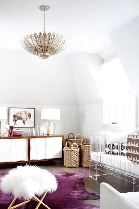 a bold contemporary nursery with an acrylic crib, a plywood credenza, baskets for storage, a purple rug and a faux fur stool