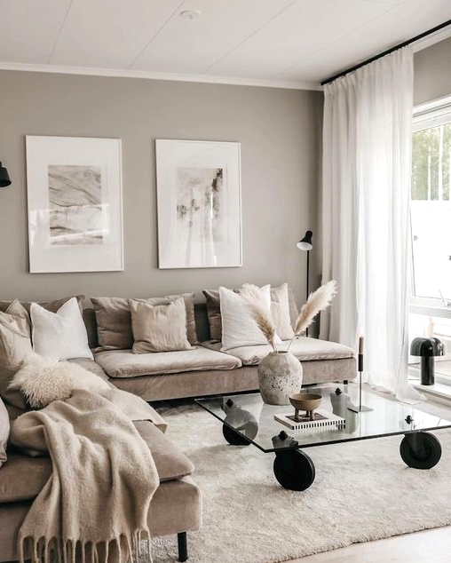 a beautiful greige living room with a cozy tan sectional, a glass table on casters, some pictures and a black sconce is a lovely idea