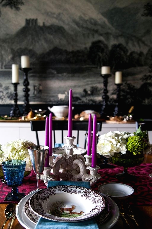 a bold and refined Thanksgiving tablescape with a purple table runner and candles, a blue napkin and glass, white blooms and greenery