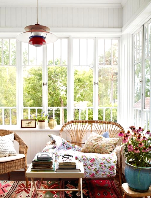 a chic boho sunroom with a colorful printed rug and other textiles, rattan and wicker furniture, potted blooms and a colorful pendant lamp