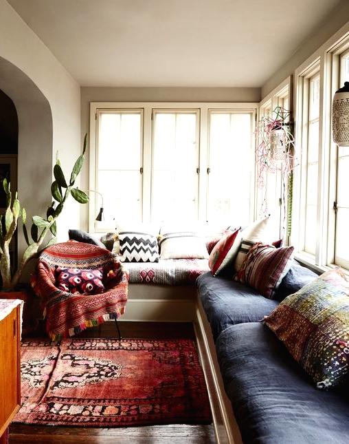 a lovely boho sunroom space with a large built-in sofa and colorful upholstery and pillows, a bold printed rug and a chair