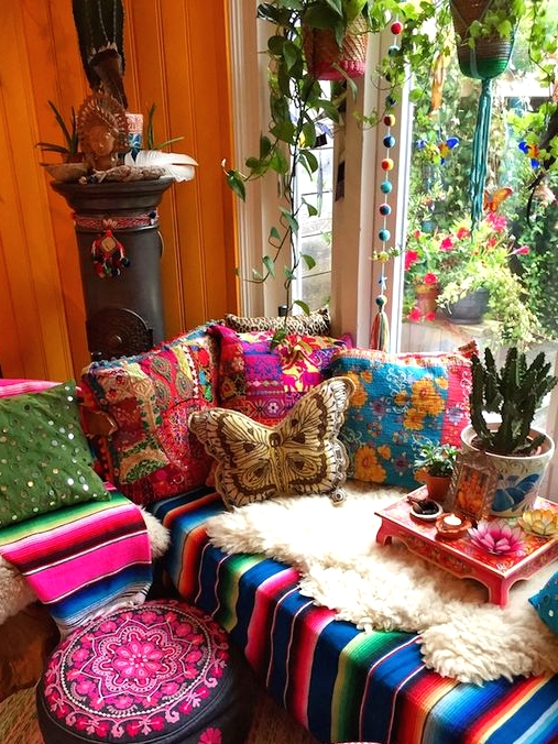 an extra colorful boho sunroom with a bright sectional, colorful pillows, blakets, ottomans, potted plants and pompoms