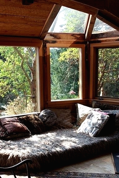 a boho sunroom with a cool forest view, a daybed right on the floor, boho rugs and a rocker chair is a very cool and bright space