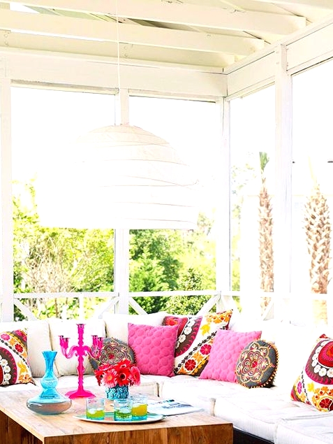 a bright boho sunroom with all white everything except for colorful and printed pillows and a rich-stained table with colorful vases