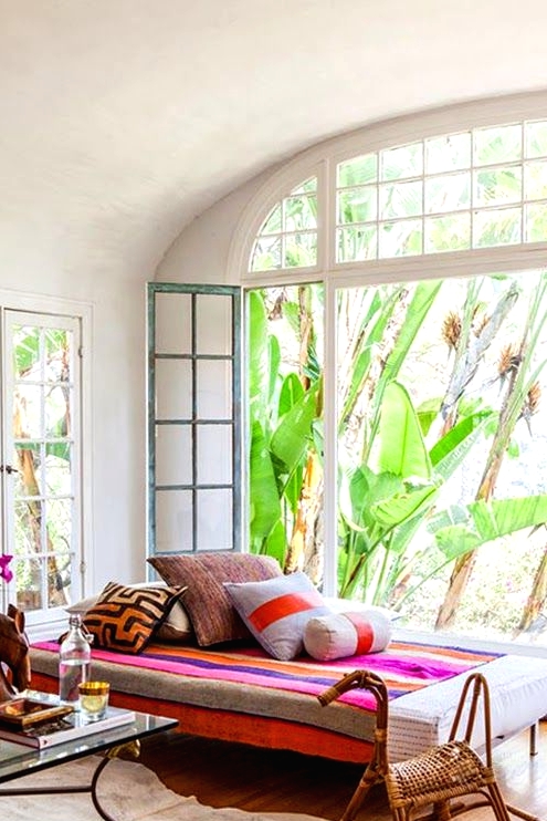 a refined colorful boho sunroom with a daybed with colorful pillows, bright blooms, a glass coffee table is very welcoming