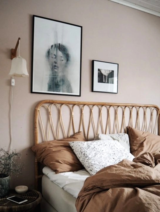 a cozy bedroom with light taupe walls, a rattan bed and a stool, a mini gallery wall and a potted plant plus sconces