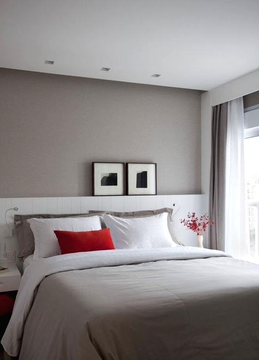a lovely small bedroom with a taupe accent wall, a bed with an extended white headboard, floating nightstands and touches of red