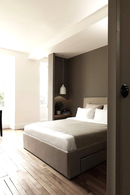 a pretty and laconic bedroom with a niche for sleeping, a taupe accent wall and a taupe bed here, a small nightstand and a pendant lamp plus a black chair