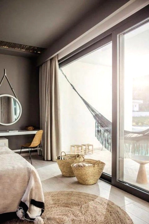 a taupe bedroom with an upholstered bed, a console taht doubles as a vanity, a round mirror and a hammock in the balcony