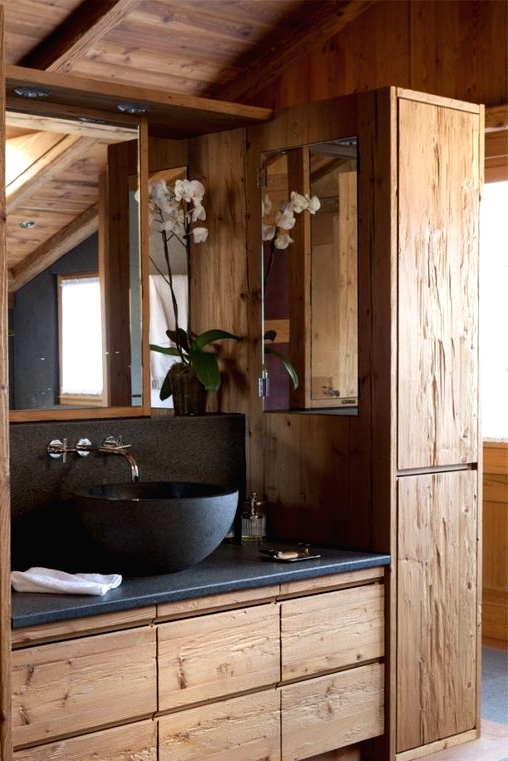 a chic chalet bathroom with plenty of textural wood, grey stone countertops, and a matching bowl sink, an orchid and a mirror