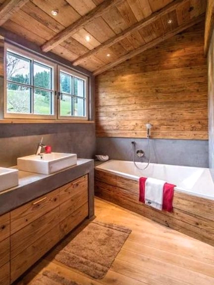 a contemporary chalet bathroom clad with wood, with wooden beams on the ceiling, a large vanity with a concrete countertops and a geometric tub