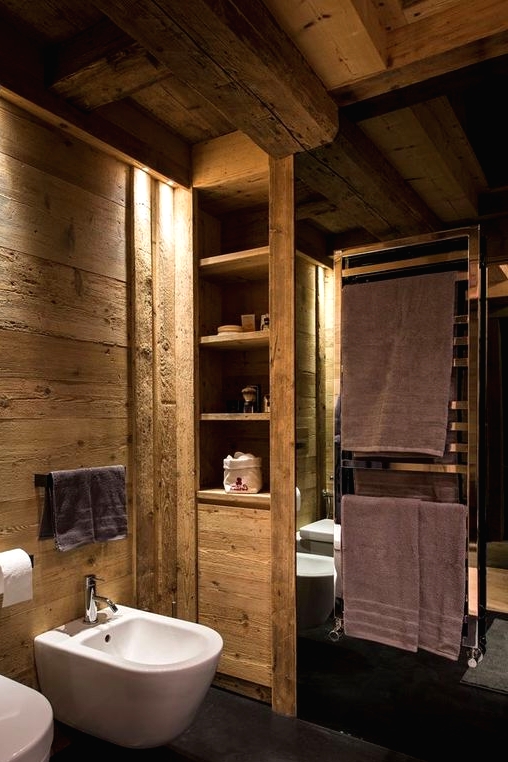 a lovely chalet bathroom clad with textural wood, with white appliances, black holders and built-in lights