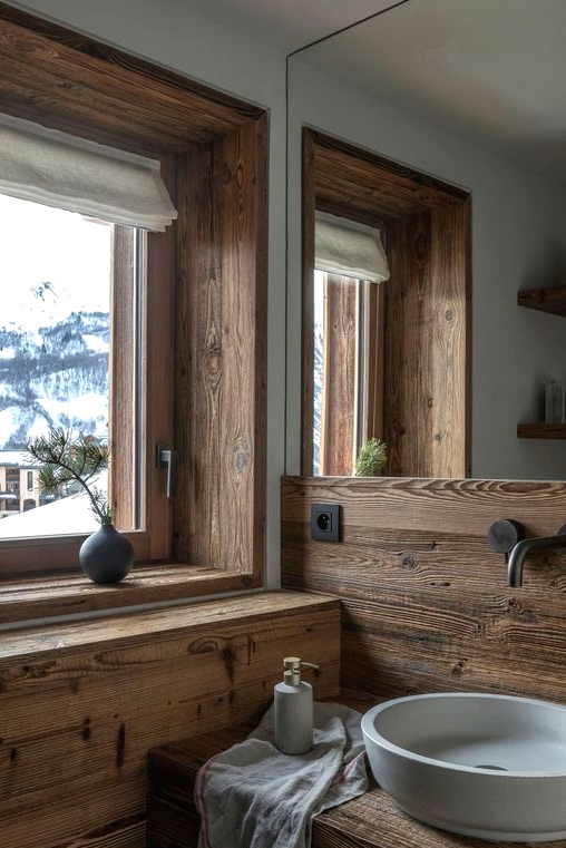 a modern bathroom clad with wood, with a window for the views, a stone sink and modern fixtures looks chic and cool