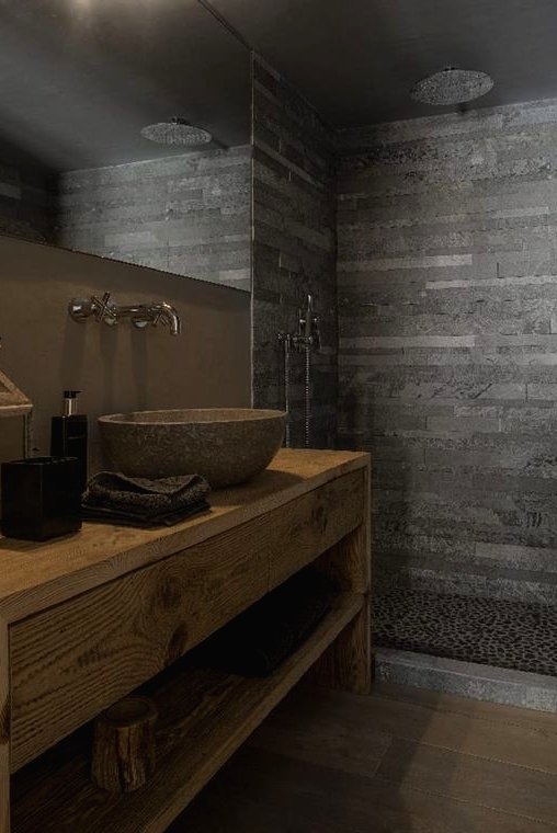 a modern chalet bathroom done with wood, stone tiles and pebbles in the shower, with a stone sink and a large mirror
