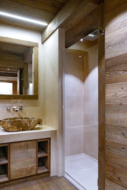 a neutral and contemporary chalet bathroom done with wood and with white concrete, with a stone sink and a mirror in a wooden frame