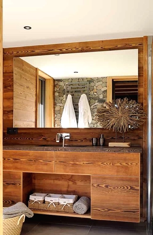 a pretty chalet bathroom clad with wood, with a built-in vanity, a large mirror, a basket for storage and a pretty artwork
