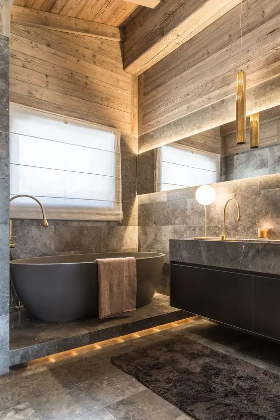 a sophisticated chalet bathroom clad with grey stone tiles, with wood, a black floating vanity with a large sink, an oval tub and lights