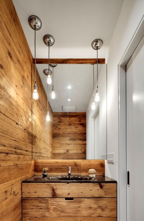 a modern bathroom with a chalet feel - a light-stained wooden wall, a matching built-in vanity, a large mirror and bulbs hanging down