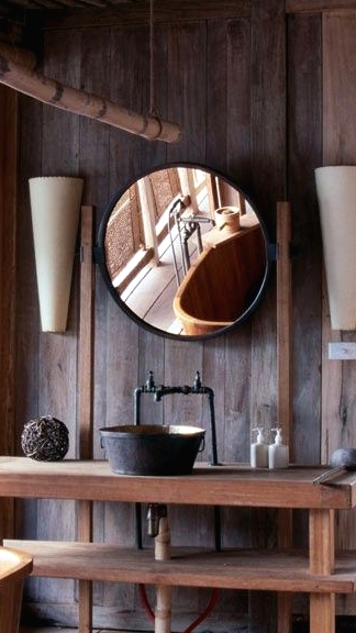 a vintage-inspired chalet bathroom clad with dark wood, with light-stained wooden pieces and a round mirror, a vintage metal sink and a faucet