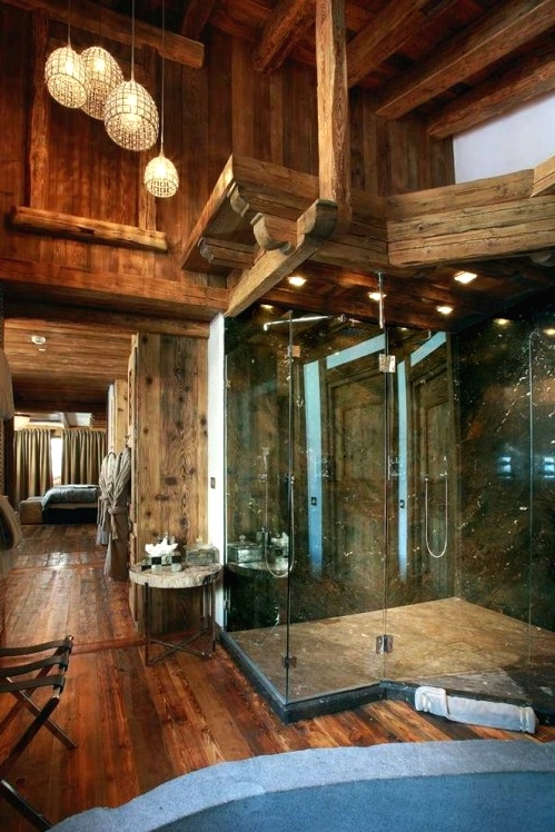 a large chalet bathroom clad with rich-stained wood, with windows, a large glass-enclosed shower and lamps