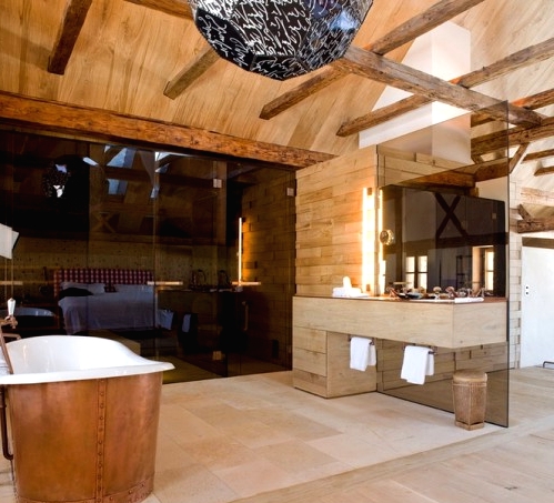 a contemporary chalet bathroom with light-stained wood wall and a ceiling, a steam room with black glass, a tub clad with copper is amazing