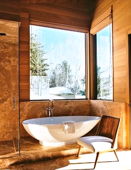 a chalet bathroom clad with light-stained wood and stone, with windows for a view, an oval tub and a glass-enclosed shower space