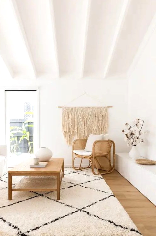 a lovely neutral boho living room with a white sofa, a woven chair and a wooden coffee table, a low built-in bench and a large macrame hanging