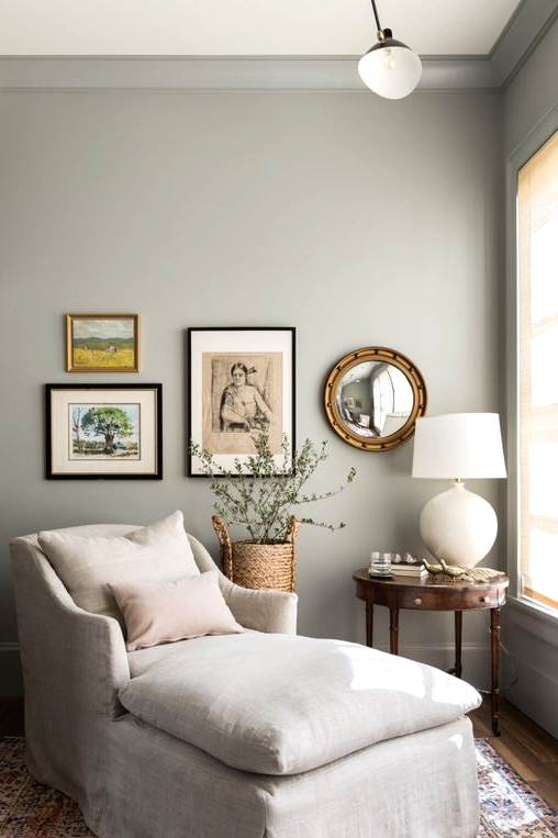 a lovely reading nook in dove grey, with a built-in bookcase, a neutral lounger, a mini gallery wall and a vintage side table