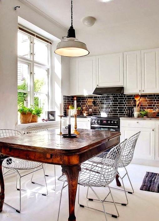 a white eat-in kitchen with a black tile backsplash, a rich-stained dining table and modern wire chairs for a contrast