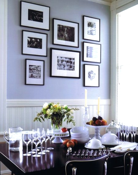 a dining room with periwinkle walls, white wainscoting, a dark-stained table and chairs, a black and white gallery wall