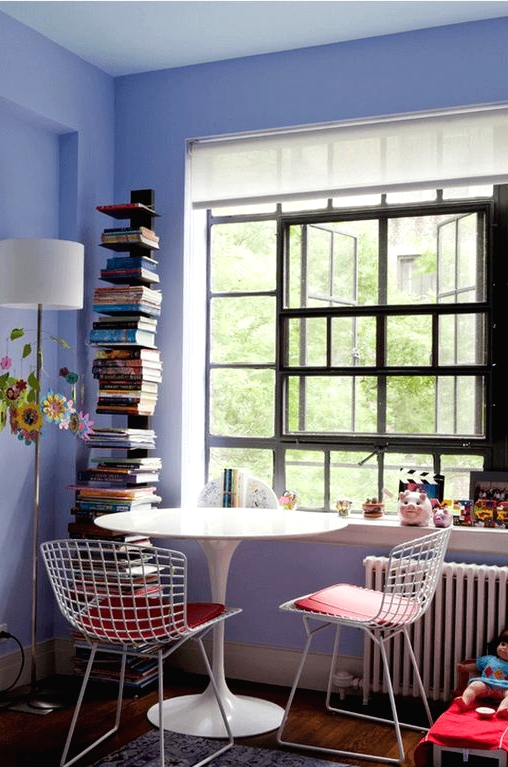 a pretty periwinkle space with a catchy window, a shelving unit, a white tale and wire chairs, a stack of books