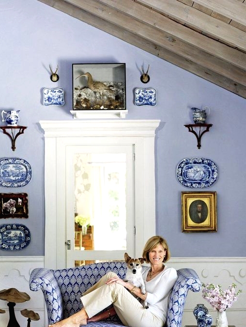 a refined vintage periwinkle space with white wainscoting, a gallery wall of plates and artworks and a printed very peri loveseat