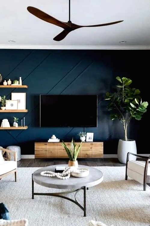 a cool living room with a navy paneled accent wall, wooden furniture, a catchy round table and greenery in pots