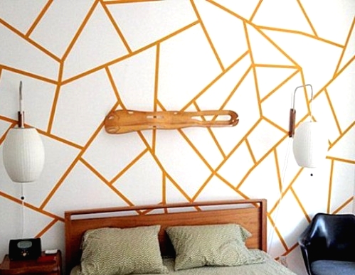 a modern bedroom with an orange and white geo print wall that takes over the whole space, a stained side table and a black chair